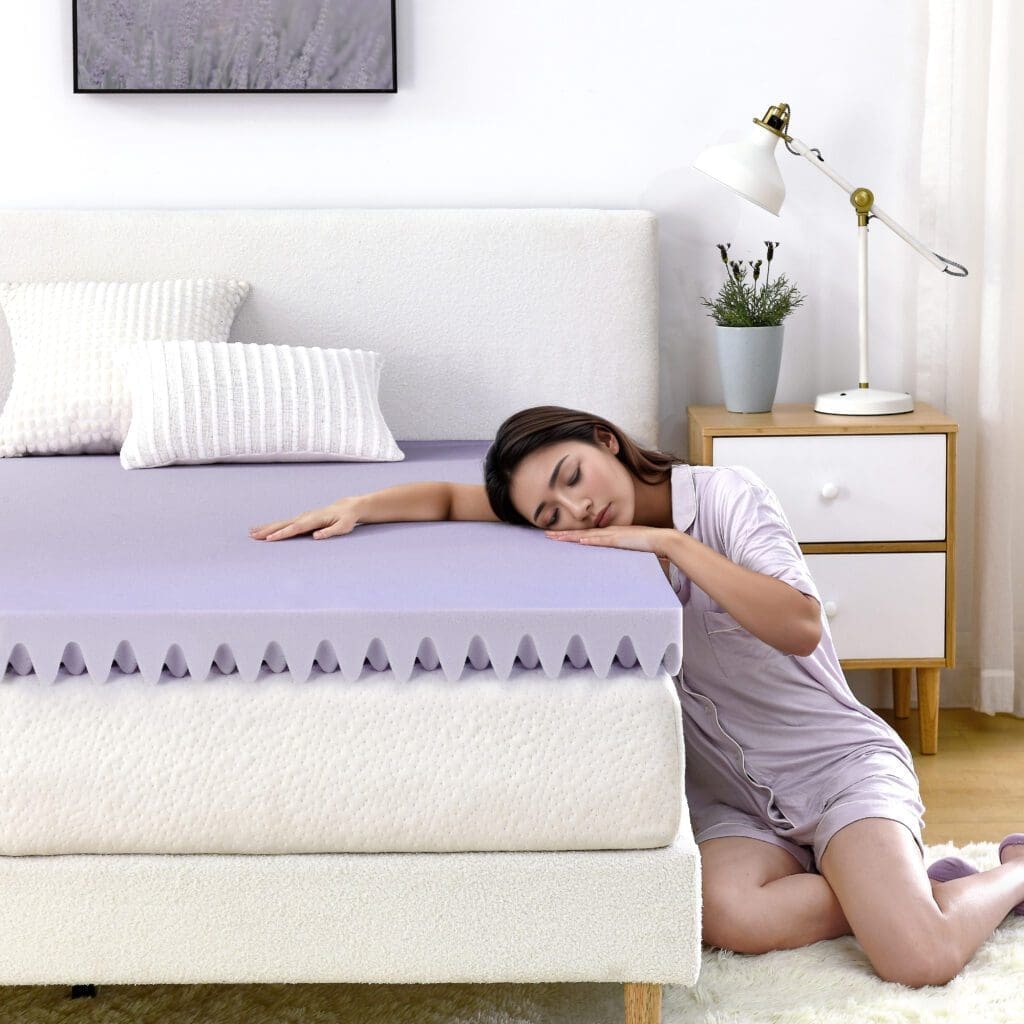 Woman sitting on the side of a bed resting her head on the mattress topper